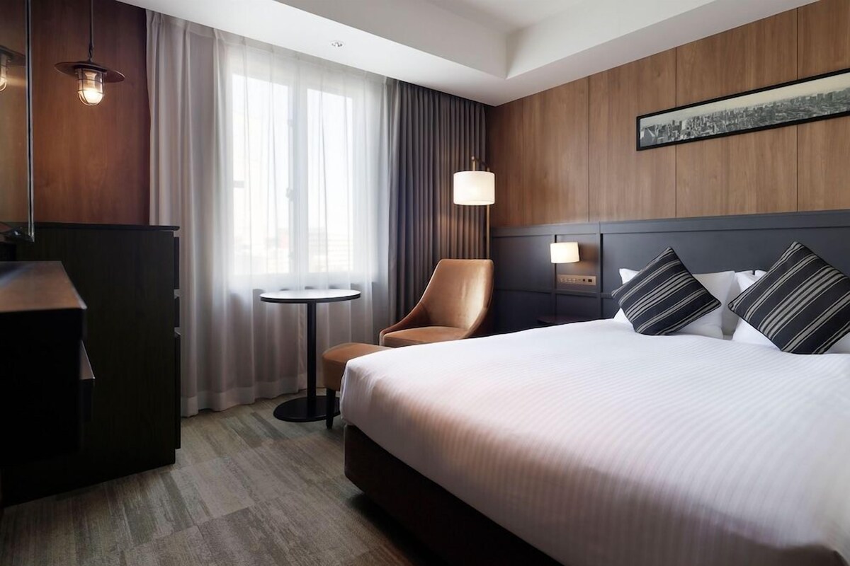 Une chambre d’hôtel avec un grand lit, un bureau, une chaise, une petite table et une lampe.