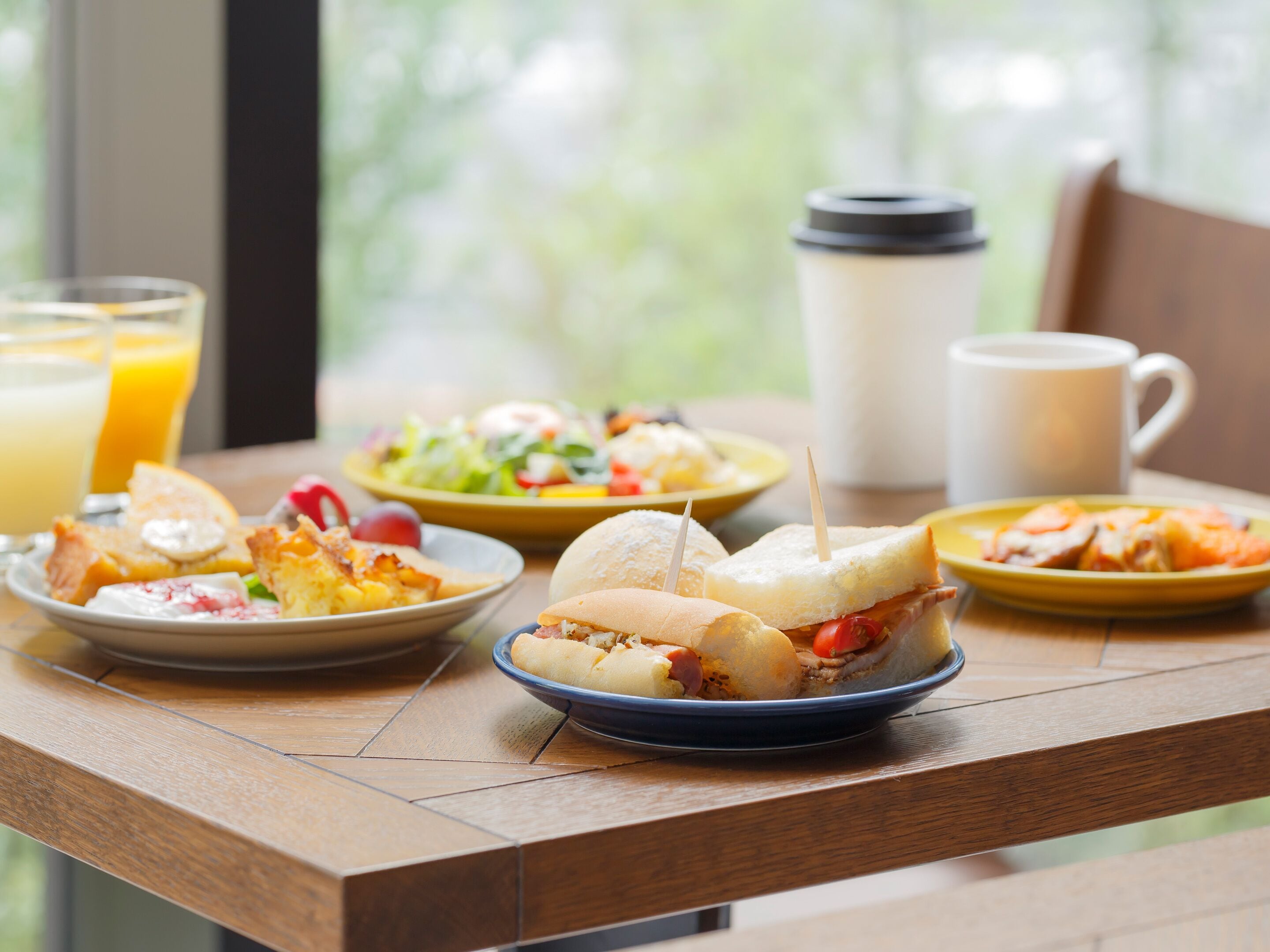 A breakfast table with various dishes, including sandwiches, a salad, and a coffee mug.