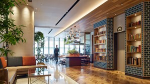 A modern interior with a wooden herringbone floor, a central seating area with a glass table, and a brick-patterned bookshelf. - Mitsui Garden Hotel Otemachi Tokyo  (Tokyo)