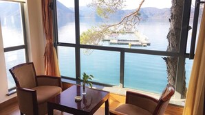 A room with a large window overlooking a lake, two chairs, a table, and a plant.