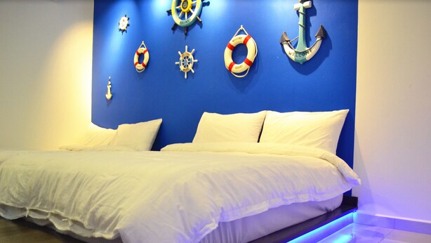 A bed with white bedding, a blue wall with nautical decor, and a blue-lit floor. - H & H Guesthouse 1 (Malacca City)
