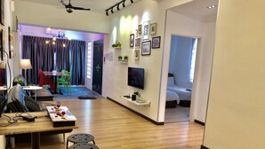 A modern living room with a wooden floor, a dining area with a table and chairs, a TV mounted on the wall, and a separate bedroom visible through an open door. - H & H Guesthouse 1 (Malacca City)