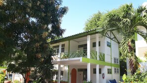 A two-story building with a green and white facade, a covered entrance, and potted plants around the entrance. - Sukhothai Bungalow (Cha-am)