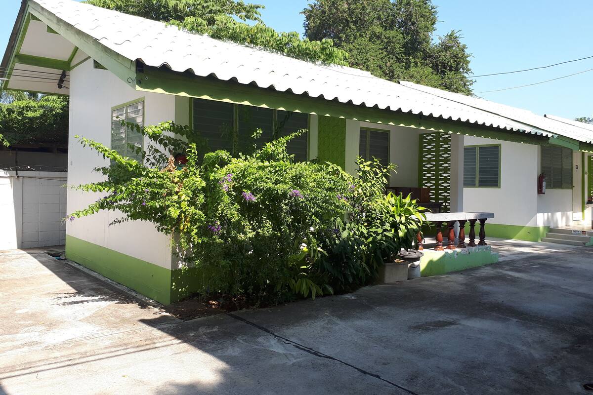 A single-story building with a green and white exterior, a tiled roof, and a small porch area with a table and chairs.