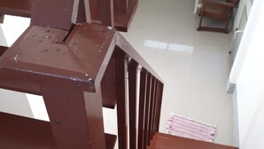 A staircase with brown railings leading to a room with a green appliance, a small table, and a patterned tablecloth. - Sukhothai Bungalow (Cha-am)
