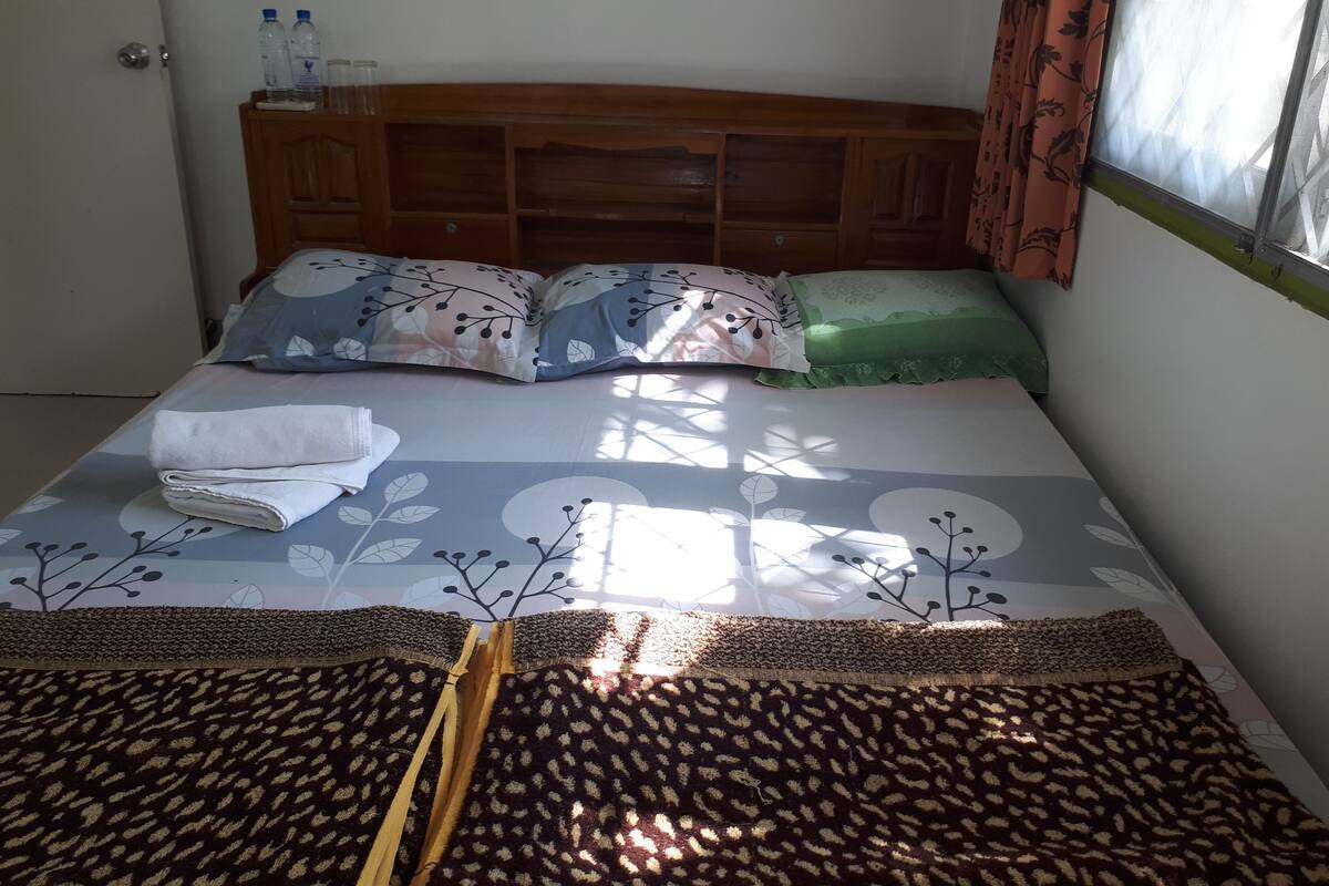 A neatly made bed with a floral bedspread, pillows, and a folded towel.