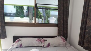 A neatly made bed with floral bedding, a rolled towel, and a window with curtains. - Sukhothai Bungalow (Cha-am)