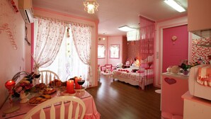 Una habitación en tonos rosados con una mesa de comedor dispuesta para una comida, una cama con ropa de cama rosa y una puerta rosada.