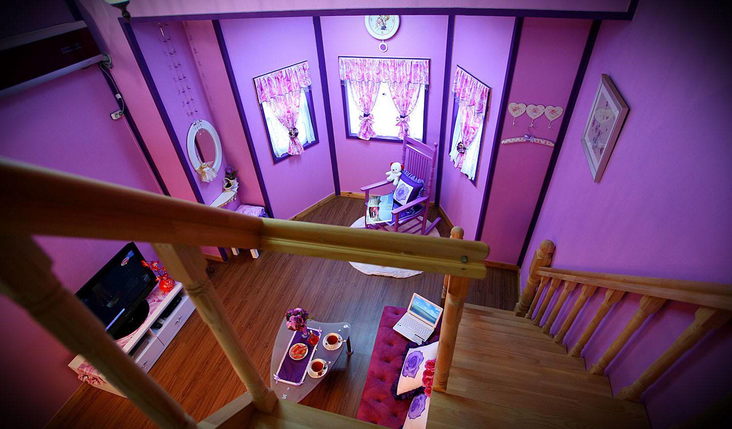A room with purple walls, a wooden staircase, a desk with a laptop, a chair, and a dining table with a teapot and cups.