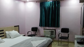 A bedroom with a bed, two chairs, a desk, a ceiling fan, and a window with curtains. - M S Hotel (Bhagalpur)