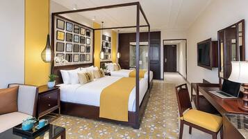 Ein Hotelzimmer mit Himmelbett, Schreibtisch, Laptop, Stuhl und Fernseher.