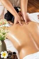 A massage therapy session with a focus on the back area, a vase with flowers, and a bottle of oil.