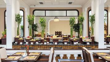 A hotel dining area with multiple buffet stations, seating arrangements, and decorative plants.