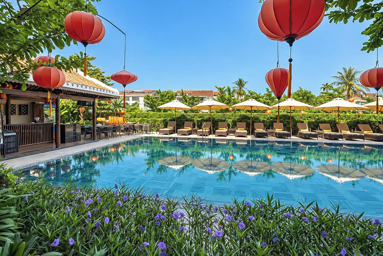 A swimming pool with lounge chairs and umbrellas, surrounded by greenery and red lanterns.