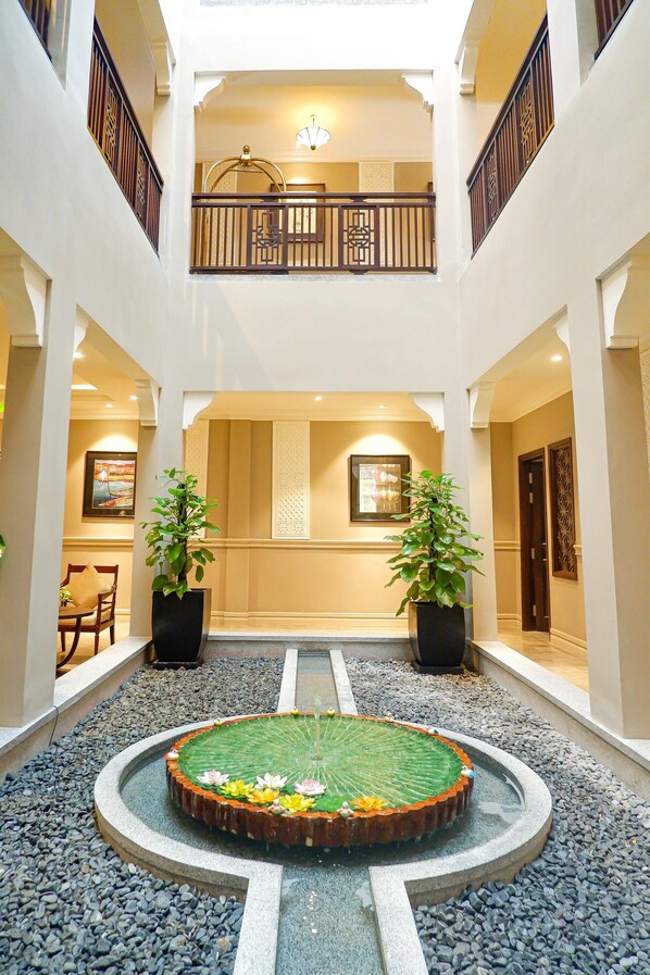 A spacious atrium with a central water feature, two potted plants, and a balcony with a railing. - Allegro Hoi An. A Little Luxury Hotel & Spa (Da Nang)