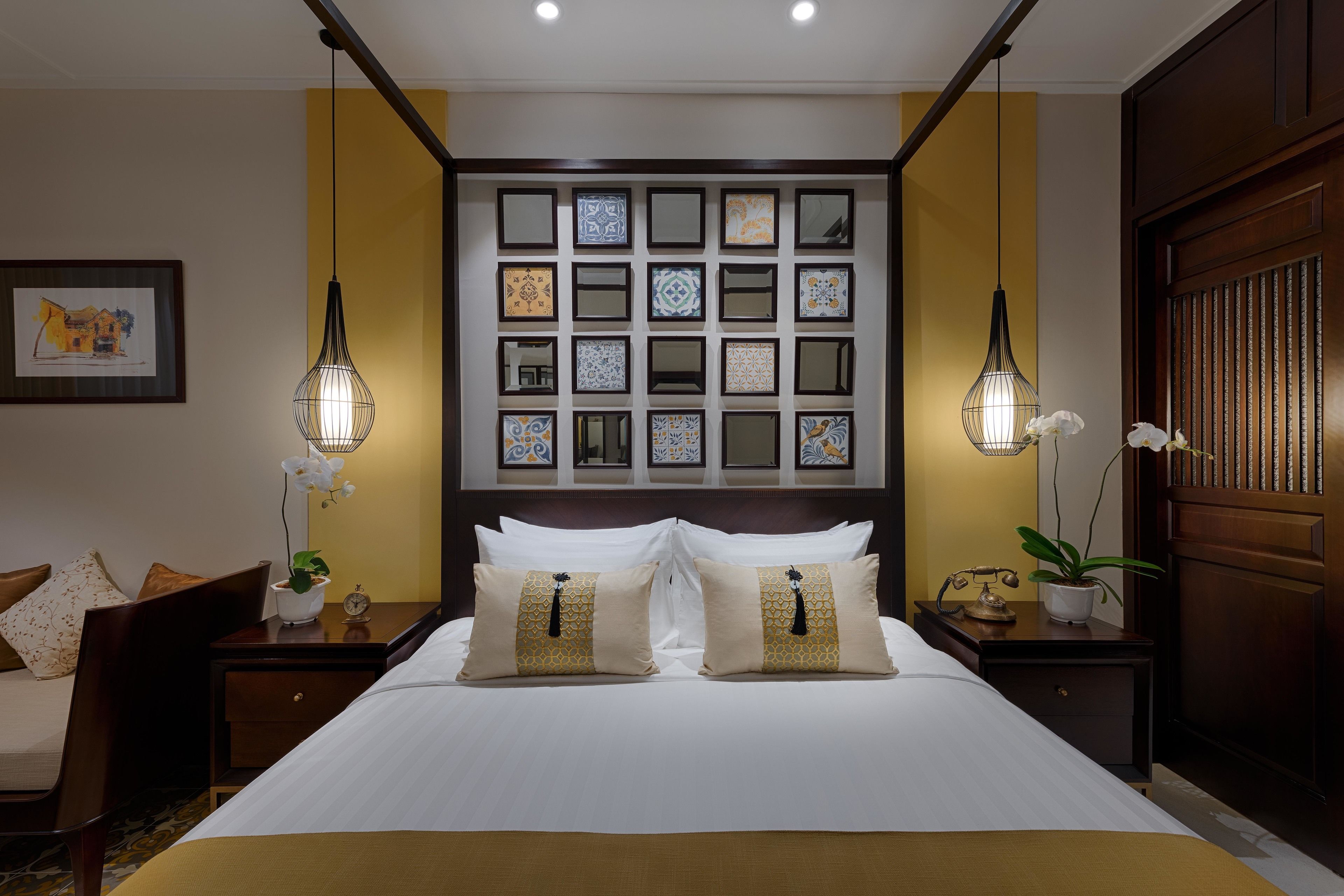 Habitación de hotel con una cama grande, dos mesitas de noche, una mesita auxiliar, un televisor montado en la pared y una obra de arte enmarcada.