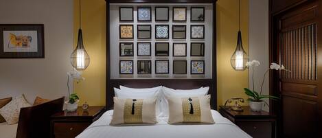 Habitación de hotel con una cama grande, dos mesitas de noche, una mesita auxiliar, un televisor montado en la pared y una obra de arte enmarcada.