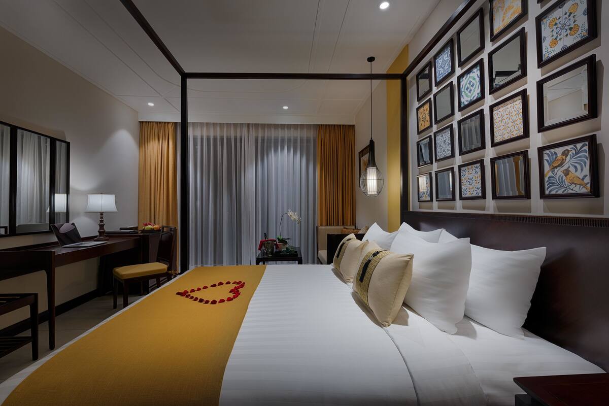 Habitación de hotel con una cama bien hecha, un escritorio con una computadora portátil, una silla y una pared decorada con cuadros.