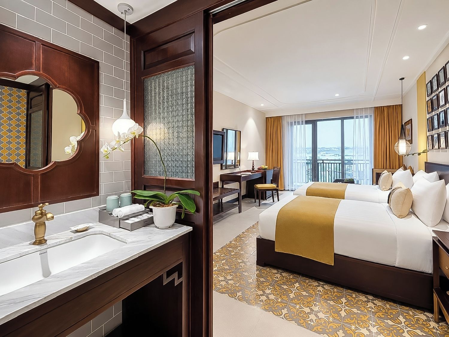 A hotel room with a large bed, a desk, a chair, a bathroom with a mirror, and a view of the city.