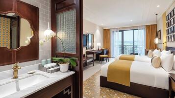 A hotel room with a large bed, a desk, a chair, a bathroom with a mirror, and a view of the city.
