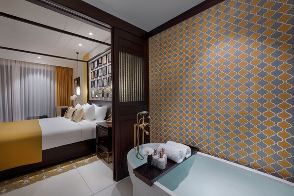 Una habitació d'hotel amb un llit, una tocador amb mirall, una banyera i una paret amb un disseny decoratiu.
