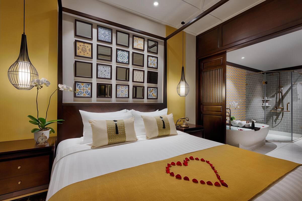 Habitación de hotel con una cama bien hecha, un ventanal con azulejos decorativos, un baño con bañera y zona de ducha.