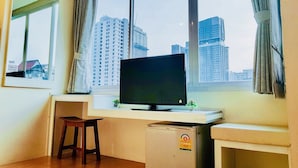 A room with a desk, a TV, a small fridge, and a window with a city view. - The Konnect Hotel (Bangkok)
