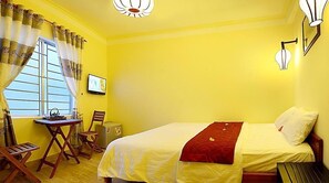 A room with yellow walls, a bed with a red blanket, a desk with a chair, and a window with curtains. - The Corner Homestay (Da Nang)