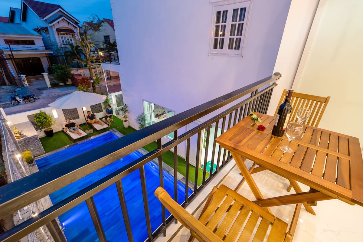 A balcony with a view of a swimming pool, wooden furniture, and a bottle of wine.