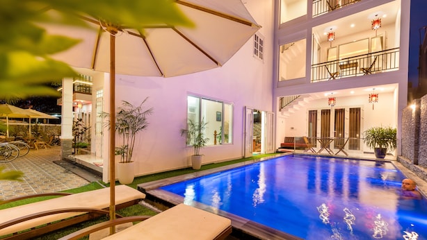A swimming pool with lounge chairs and umbrellas, surrounded by potted plants and a building with balconies. - Horizon Homestay (Da Nang)