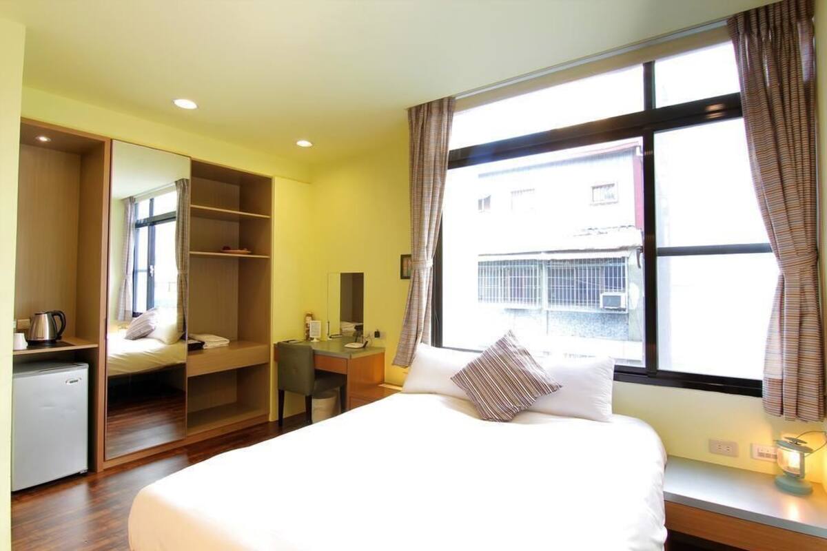 A hotel room with a bed, a desk, a chair, a wardrobe, and a window.