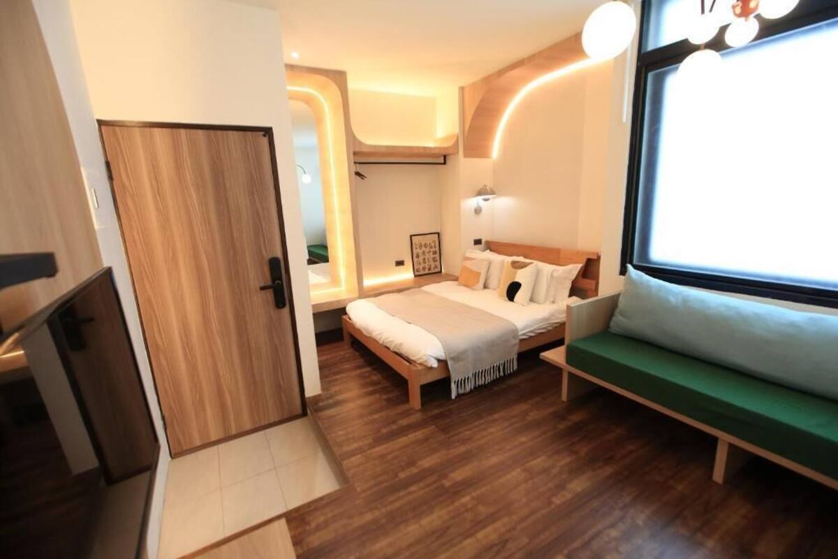 A modern bedroom with a wooden floor, a bed with white bedding, a green sofa, and a large window with a view.