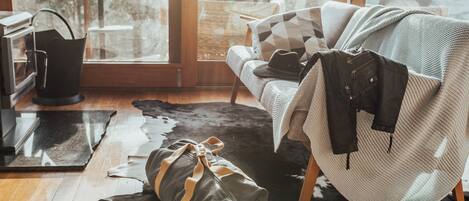 A cozy room with a wooden floor, a leather sofa, a patterned throw, and a large window with a view.