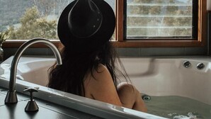 A person sitting in a bathtub with a view of a landscape through a window. - Kangaroo Ridge Retreat (Healesville)