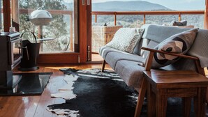 A cozy living room with a sofa, a coffee table, and a view of the mountains through large windows. - Kangaroo Ridge Retreat (Healesville)