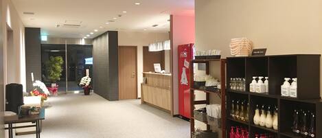 A hotel lobby with a reception desk, a Coca-Cola refrigerator, and shelves stocked with toiletries.
