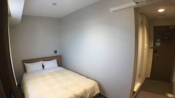 Habitación de hotel con una cama individual, cabecera de madera y pared blanca.