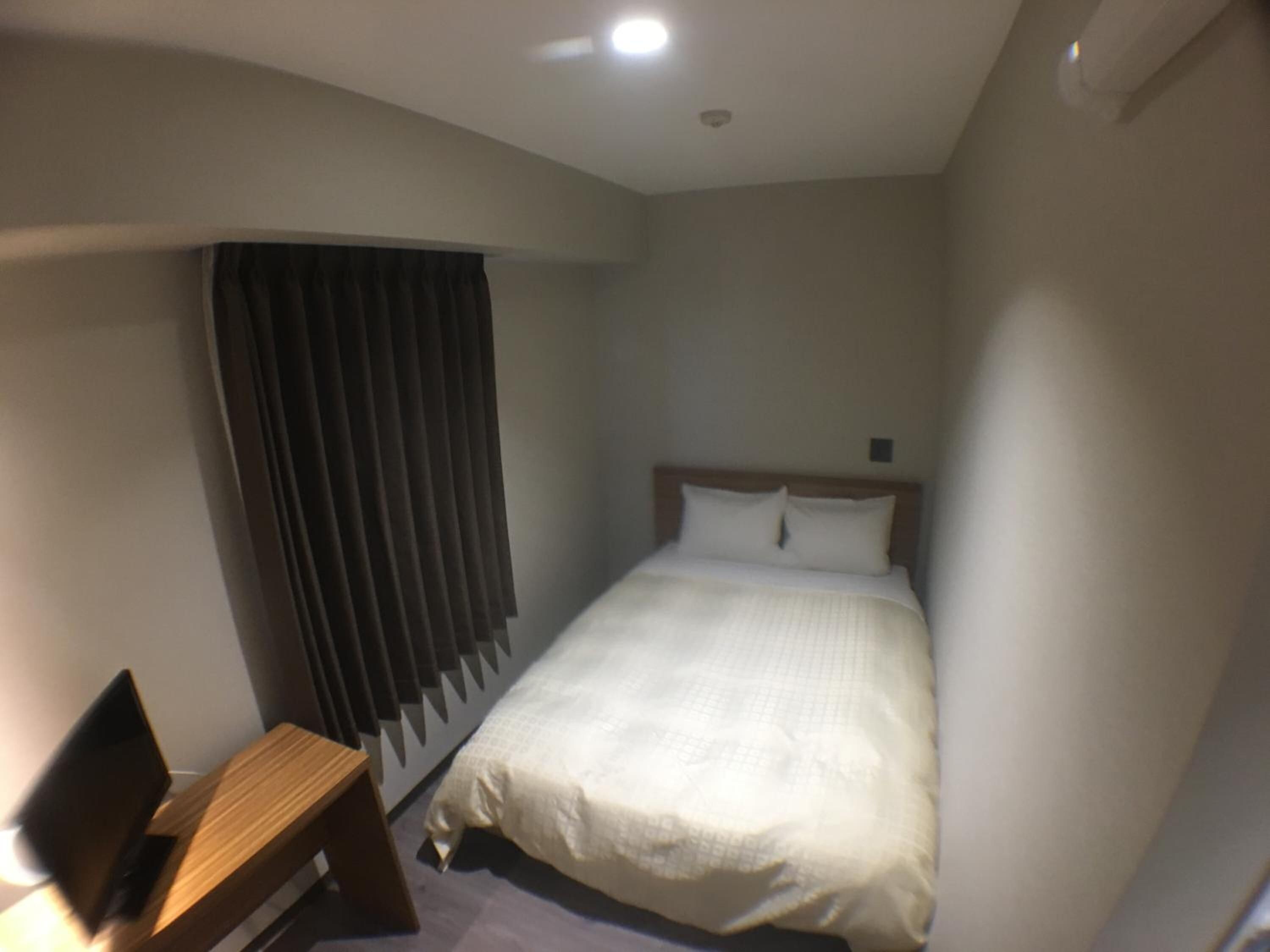 A hotel room with a single bed, a bedside table, and a window with curtains.
