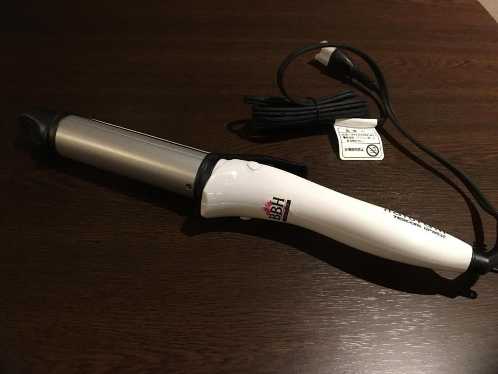 A curling iron with a cord and a power adapter on a wooden surface.