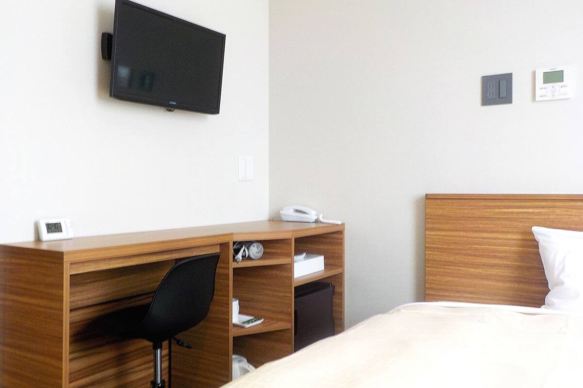 Une chambre d’hôtel équipée d’un lit, d’un bureau avec une chaise, d’une télévision, d’un téléphone et d’un thermostat.