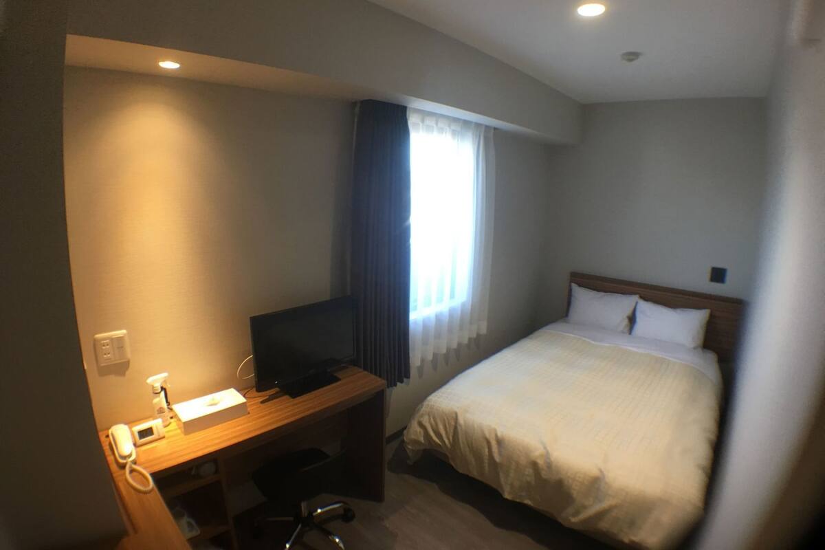 Une chambre d’hôtel avec un lit, un bureau équipé d’un ordinateur, un téléphone et une fenêtre avec des rideaux.
