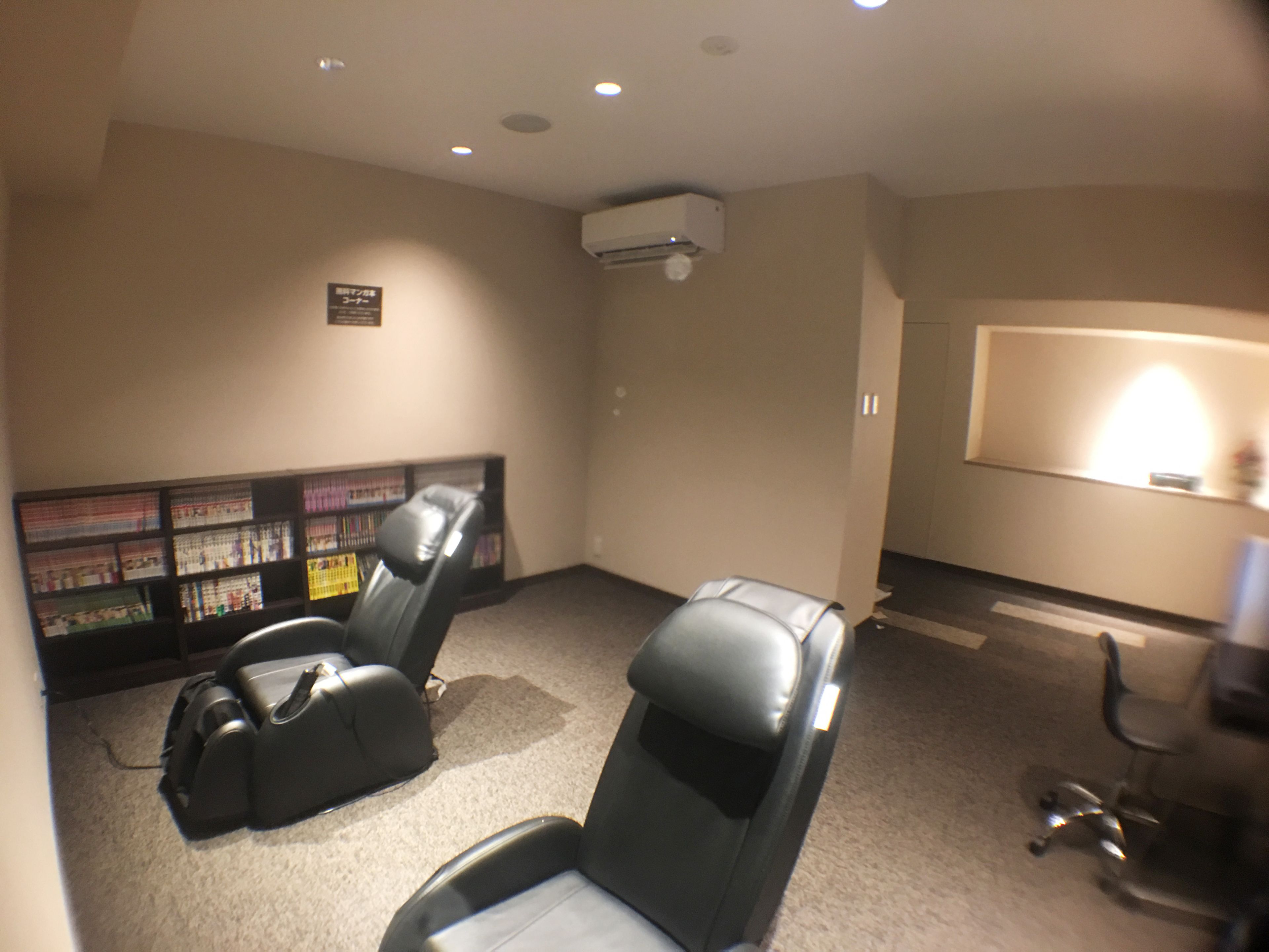 A home theater room with two reclining chairs, a bookshelf, and an air conditioning unit.
