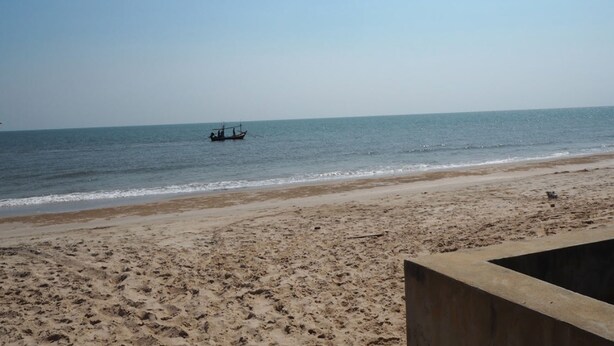 A beach with a boat in the water and a concrete structure on the sand. - Baan Tukta at Beach (Cha-am)