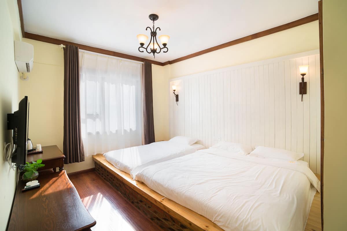 A hotel room with two beds, a wooden bench, a TV, and a plant.