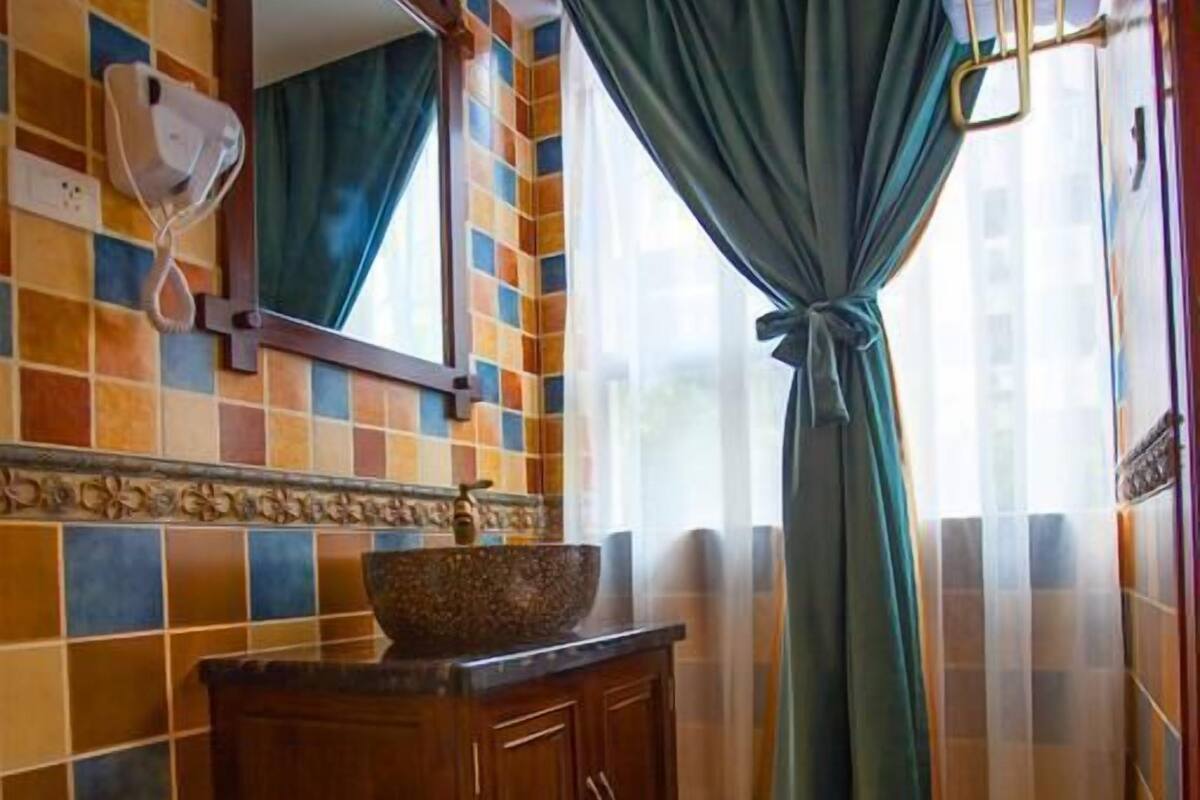 A bathroom with a tiled floor, a wooden vanity, a large mirror, and a window with curtains.