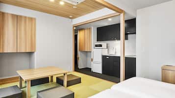 Ein kleines Hotelzimmer mit Holzbalkendecke, einer Küchenzeile, einem Bett und einem Tisch mit Sitzgelegenheit.