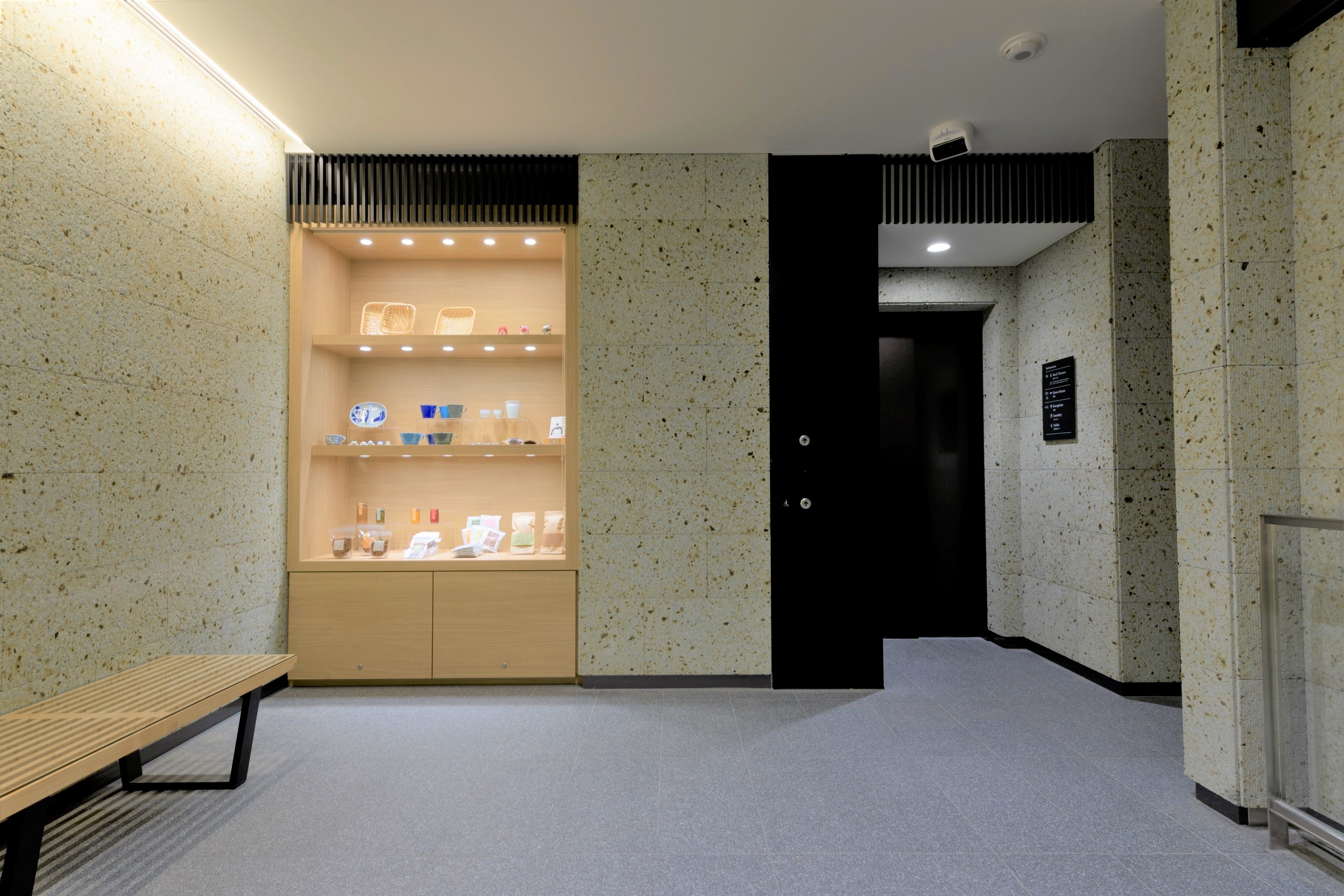A hallway with a bench, a display case with items, and a door.