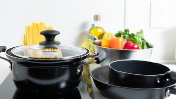 A kitchen with a black electric stove, a pot with a lid, a pan, and a bowl of vegetables.