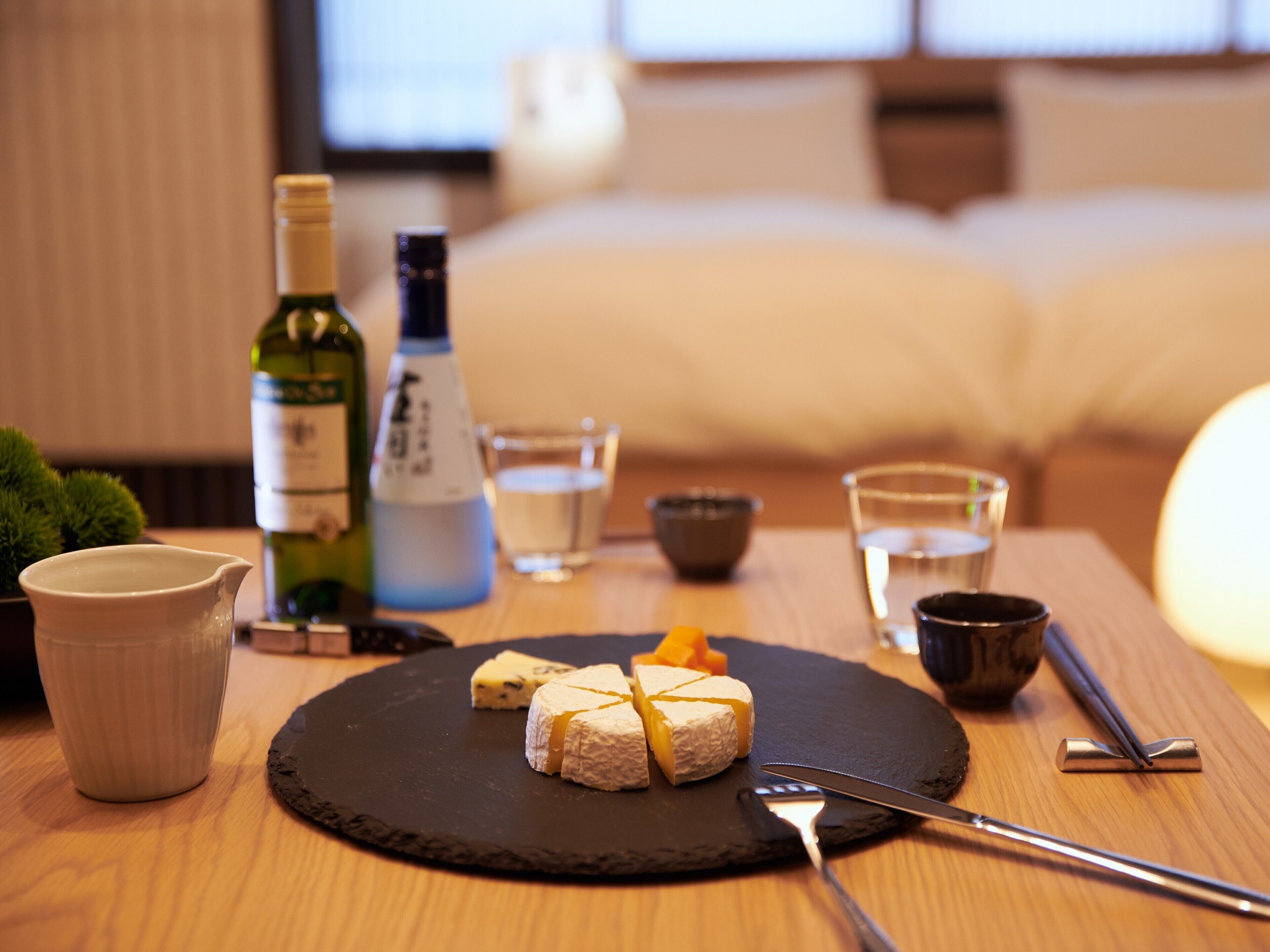 A table with a cheese platter, a bottle of wine, glasses, and a cup.