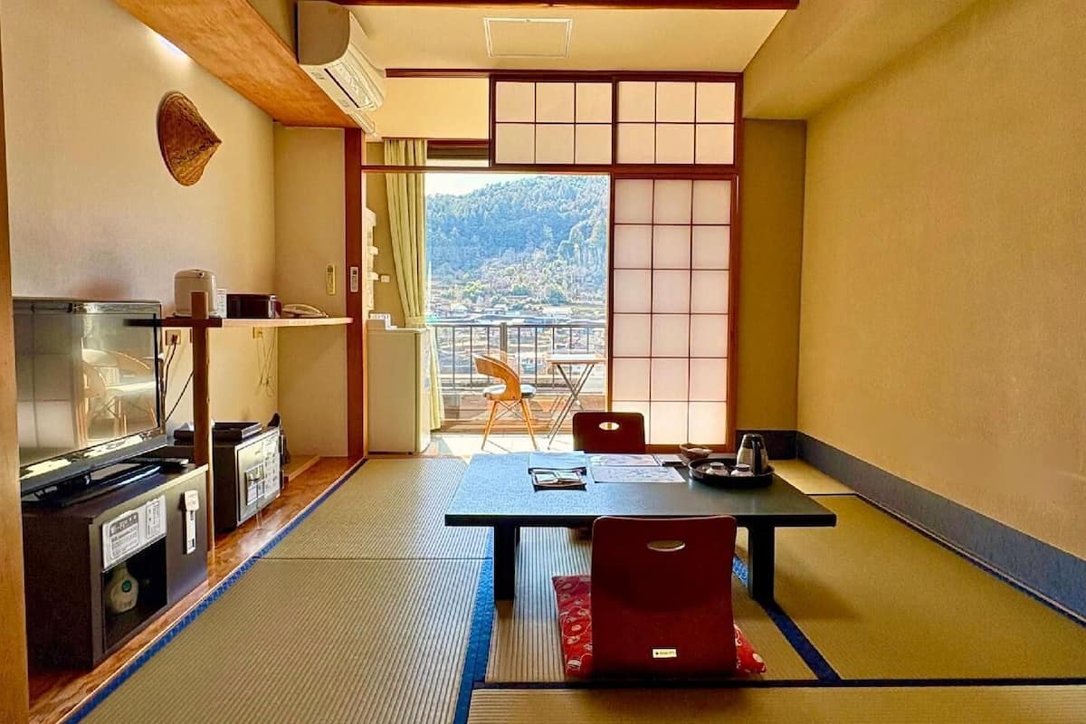 A traditional Japanese room with tatami flooring, a low table, a sofa, and a view of a mountainous landscape through a sliding door.